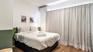 A neatly made bed with white linens, a bedside lamp, and a wall-mounted air conditioner. - 360 Ver.de Panorama  (São Paulo)