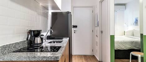 A compact hotel room with a kitchenette, a bed, and a small seating area.