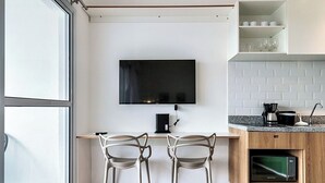 A modern kitchen with a flat-screen TV mounted above a wooden counter, two chairs, and a microwave. - 360 Ver.de Panorama  (São Paulo)