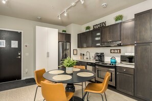 Une cuisine moderne avec des meubles en bois foncé, un réfrigérateur en acier inoxydable, une machine à café et un coin repas comprenant une table ronde et deux chaises.