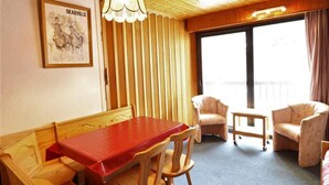 Ein Zimmer mit Holzboden, einem Esstisch mit Stühlen, einer Couch und einem großen Fenster mit Vorhängen.