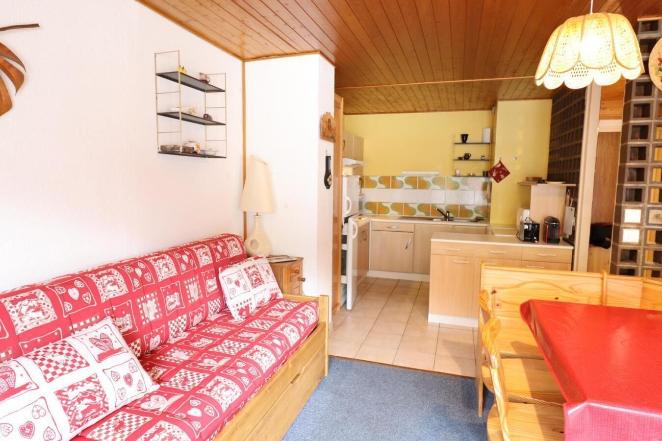 Ein gemütlicher Raum mit einem rot gemusterten Sofa, einem Holzesstisch und einer Küchenzeile mit gefliestem Rücksprühefeld und Holdekor.