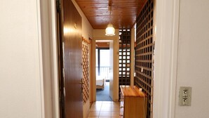 Ein schmaler Flur mit einer Holztür, einer Holzbank und einer Wand mit Gittermuster.