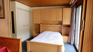 Ein Schlafzimmer mit einem Holzbett, eingebautem Kleiderschrank und einem Fenster mit Vorhängen.