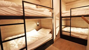 A room with bunk beds, wooden walls, and a small light fixture.