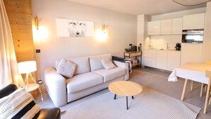 A modern living room with a sofa, a small round table, and a kitchen area with cabinets and a dining table.