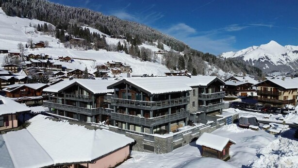 A snow-covered mountain resort with chalet-style buildings, ski slopes, and a clear blue sky.