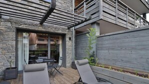 A patio with two reclining chairs, a table, and a stone wall.