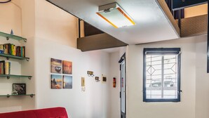 A red sofa, a glass table with a book and a potted plant, and a window with a view of parked cars. - Catania City Apartment by Wonderful Italy (Catania)