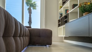 A modern living room with a sofa, a bookshelf, and a view of a palm tree outside.