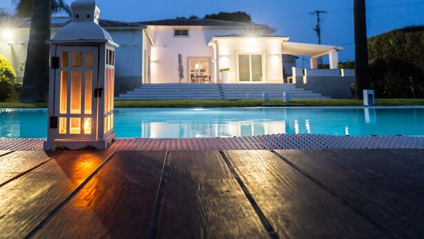 A modern house with a swimming pool, a lantern, and palm trees.