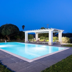Una piscina con una pérgola blanca y sillas de descanso.