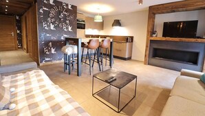 A modern living room with a sofa, a coffee table, and a TV. There is a kitchen area with a dining table and chairs. - Wifi, 200m from ski slopes, 1st floor, balcony, 65m², Les Gets (Les Gets)