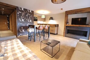 A modern living room with a sofa, a coffee table, and a TV. There is a kitchen area with a dining table and chairs. - Wifi, 250m from resort center, 1st floor, balcony, 65m², Les Gets (Les Gets)