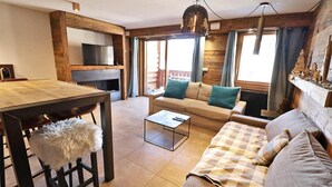 A cozy living room with a wooden dining table, a sofa, a coffee table, and a television. - Wifi, 200m from ski slopes, 1st floor, balcony, 65m², Les Gets (Les Gets)