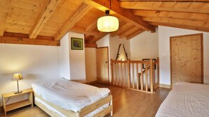 Um quarto de madeira com uma cama, uma mesinha de cabeceira, um candeeiro pendente e uma porta de madeira.