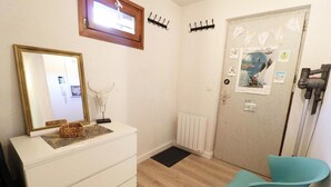 A room with a white dresser, a mirror, a small table with decorative items, a teal chair, a radiator, and a door with various posters. - Balcony, 28m², Les Gets (Les Gets)