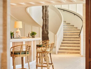 A modern interior with a curved staircase, a bar area with wicker chairs, and a wooden column.