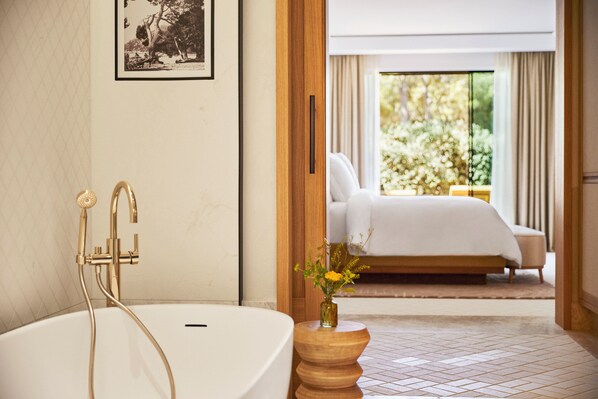 A modern bathroom with a freestanding bathtub, a wooden side table with a vase, and a framed picture on the wall.