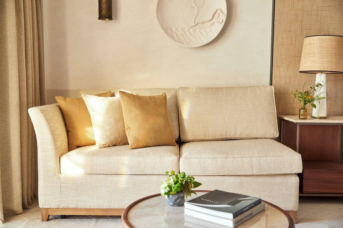 A beige sofa with three cushions, a small plant on a round table, and a lamp on a side table.