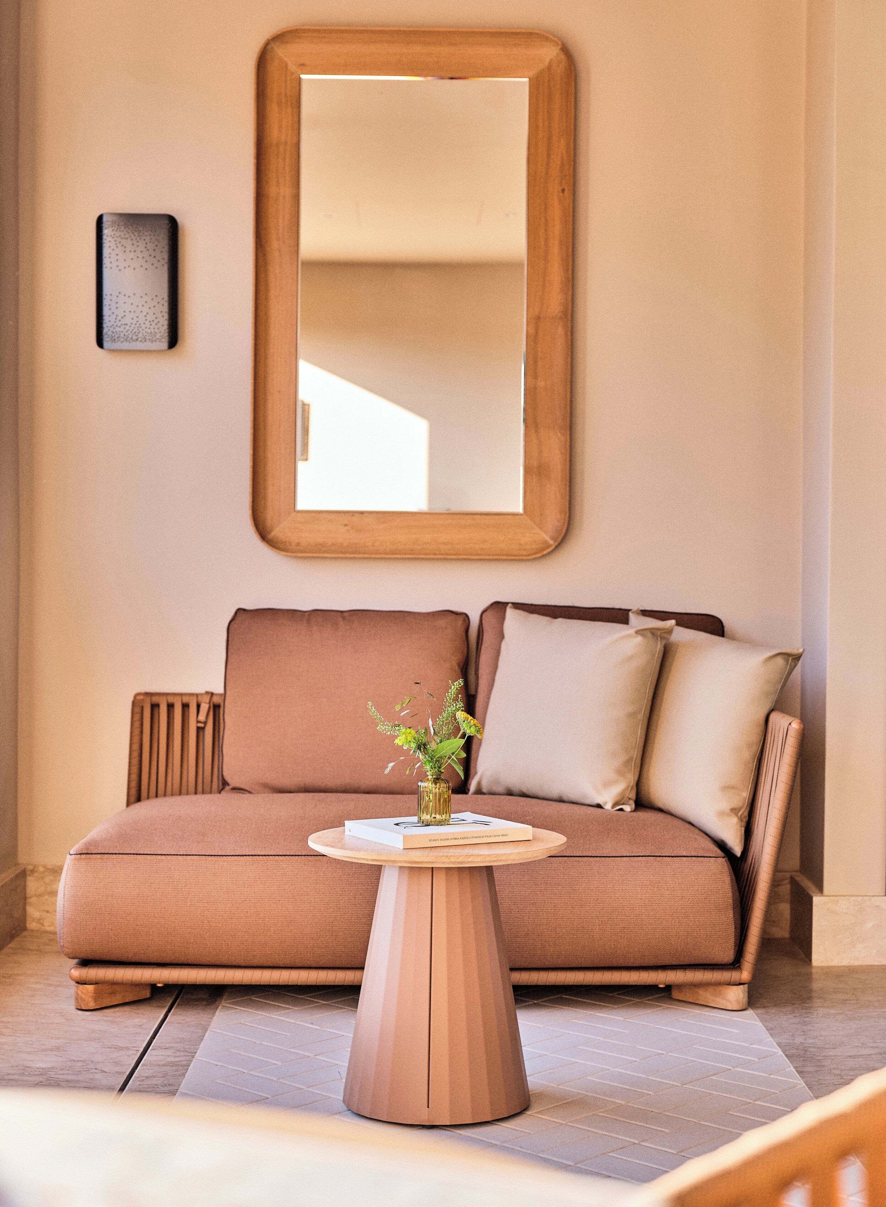 Una sala moderna con un sofá, una mesa redonda de madera y un espejo grande en la pared.