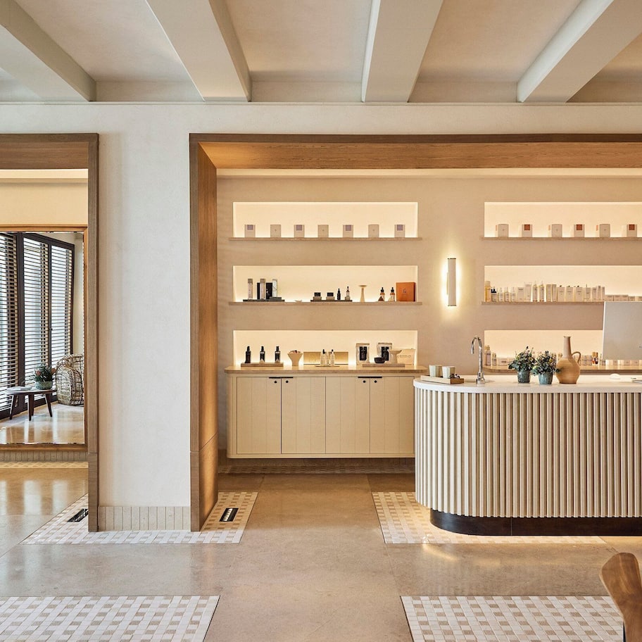 A modern reception area with a central desk, multiple shelves with items, and a view into a dining area.