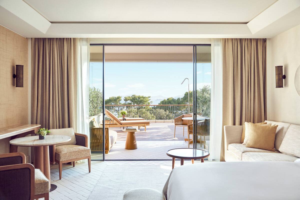 A modern hotel room with a balcony, a sofa, a dining table, and a bed.