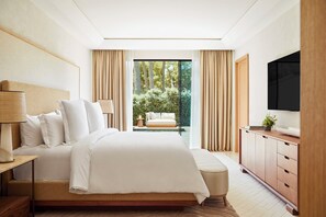 A modern hotel room with a large bed, a television, a wooden cabinet, and a view of a pool and greenery.