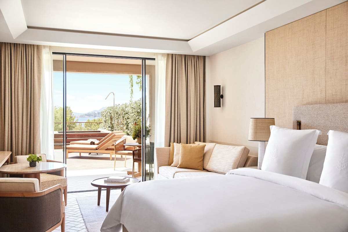 A hotel room with a large bed, a sofa, a dining area, and a balcony with a view of the mountains.