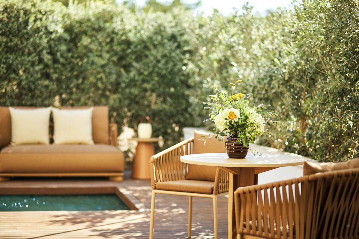 An outdoor seating area with a wooden table, wicker chairs, and a sofa with cushions.
