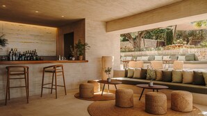 Un bar moderno con taburetes, una barra repleta de botellas y un área de estar con cojines y sofá.
