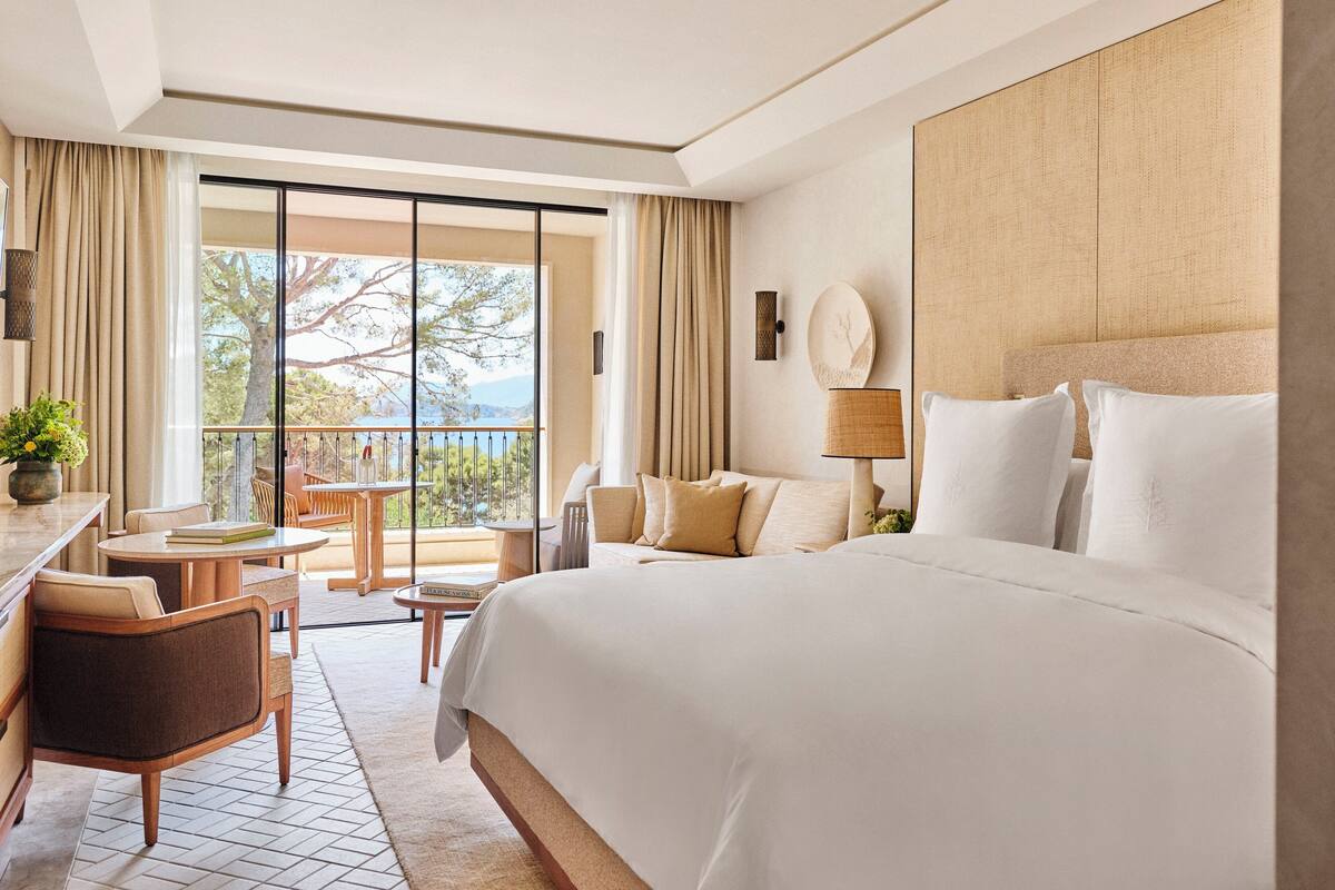 A hotel room with a large bed, a desk, a chair, and a balcony with a view of the outdoors.