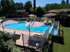 A rectangular swimming pool with a white fence, two umbrellas, and lounge chairs.