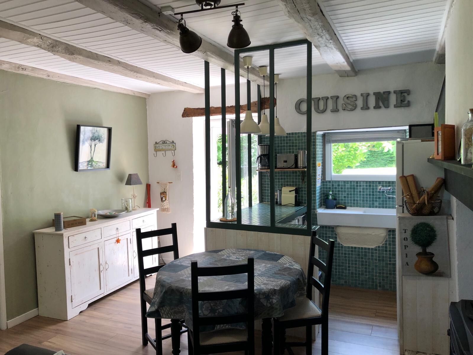 Een landelijke keuken met een eettafel, stoelen, een hanglamp en een raam met uitzicht op groen.