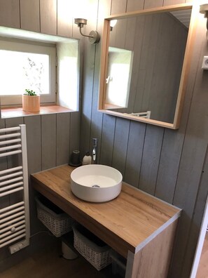 A bathroom with a wooden vanity, a round sink, a mirror, a towel rack, and a window with a plant.