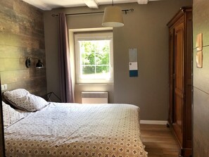 A bedroom with a bed, a window, a hanging light, and a wooden wardrobe.