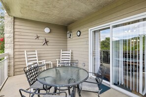 A covered patio area with a round glass table and four chairs, a clock, and a star decoration on the wall.