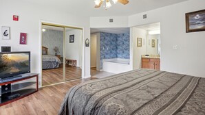 A bedroom with a bed, a ceiling fan, a television, and a bathroom with a bathtub. - 3 BR | Indoor Pool/Hot Tub | Balcony | Free Tickets (Pigeon Forge)