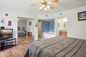 A bedroom with a bed, a ceiling fan, a television, and a bathroom with a bathtub.