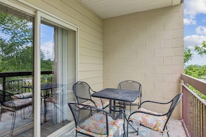 A balcony with a table and chairs, a glass door, and a view of trees.