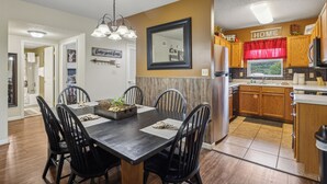 A modern kitchen with wooden cabinets, a stainless steel refrigerator, and a dining area with a dark wooden table and chairs. - Stay on the River, Steps from Dolly Parton’s Stampede – Charming 2BR Retreat (Pigeon Forge)