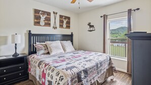A bedroom with a bed, a nightstand, a lamp, a ceiling fan, and wall art. - Stay on the River, Steps from Dolly Parton’s Stampede – Charming 2BR Retreat (Pigeon Forge)