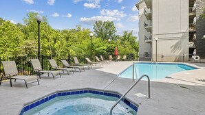 A pool area with lounge chairs, a hot tub, and a building in the background. - Stay on the River, Steps from Dolly Parton’s Stampede – Charming 2BR Retreat (Pigeon Forge)