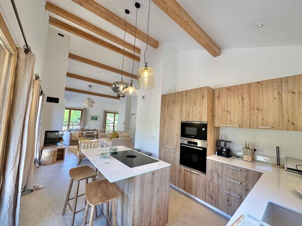 Une cuisine moderne avec des meubles en bois, un îlot central doté de tabourets et un éclairage suspendu.