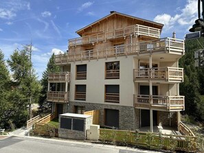 Un immeuble à plusieurs étages, doté de balcons, d’une façade en pierre et offrant une vue sur les arbres.