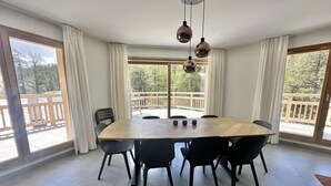 A spacious dining area with a large wooden table surrounded by black chairs, large windows with curtains, and a view of a wooden deck outside. - 3rd floor, sauna, balcony, tv, ski locker, 115m², Vars (Vars)