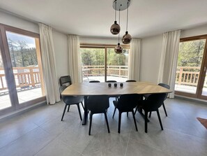 Tilava ruokailutila, jossa on suuri puinen pöytä, jonka ympärillä on mustia tuoleja, suuret ikkunat, joissa on verhot, ja näkymä ulkona olevalle puukannelle.