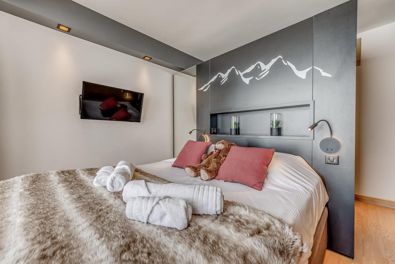 Een moderne slaapkamer met een groot bed, een zacht tapijt en een aan de muur bevestigde televisie.