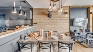 A modern kitchen with a wooden accent wall, a dining area with a white furry rug, and a TV mounted on the wall. - 200m from ski slopes, 5th floor, view mountain, balcony, ski locker, 50m², Tignes (Tignes)