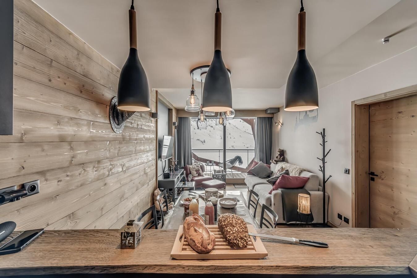 A modern kitchen with wooden accents, a dining area, and a view of a snowy landscape.